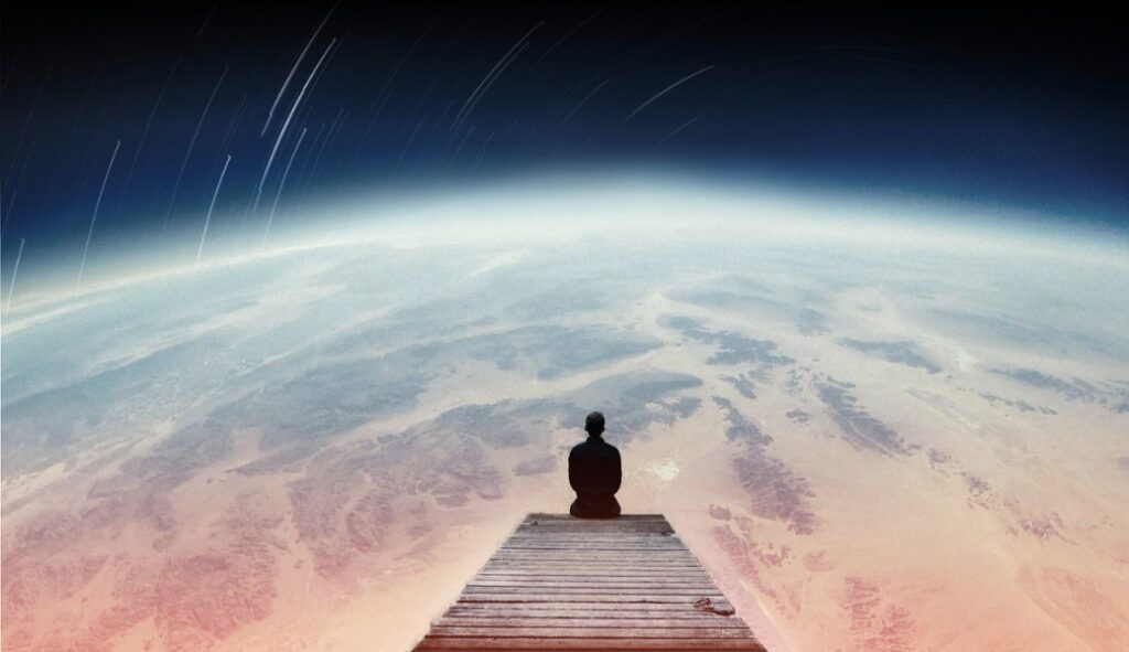 Homem solitário sentado sobre uma plataforma de madeira observando a Terra do espaço, simbolizando a conexão entre o humano e o cosmos e pensando no Paradoxo de Fermi